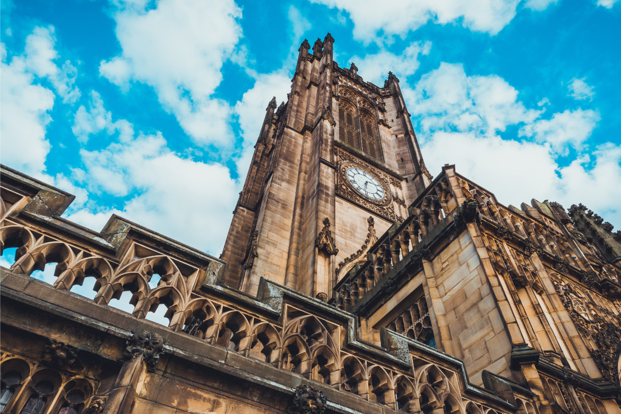 Manchester Cathedral clock tower under blue sky – local landmark representing Shahs Logistics courier and delivery services in Manchester.